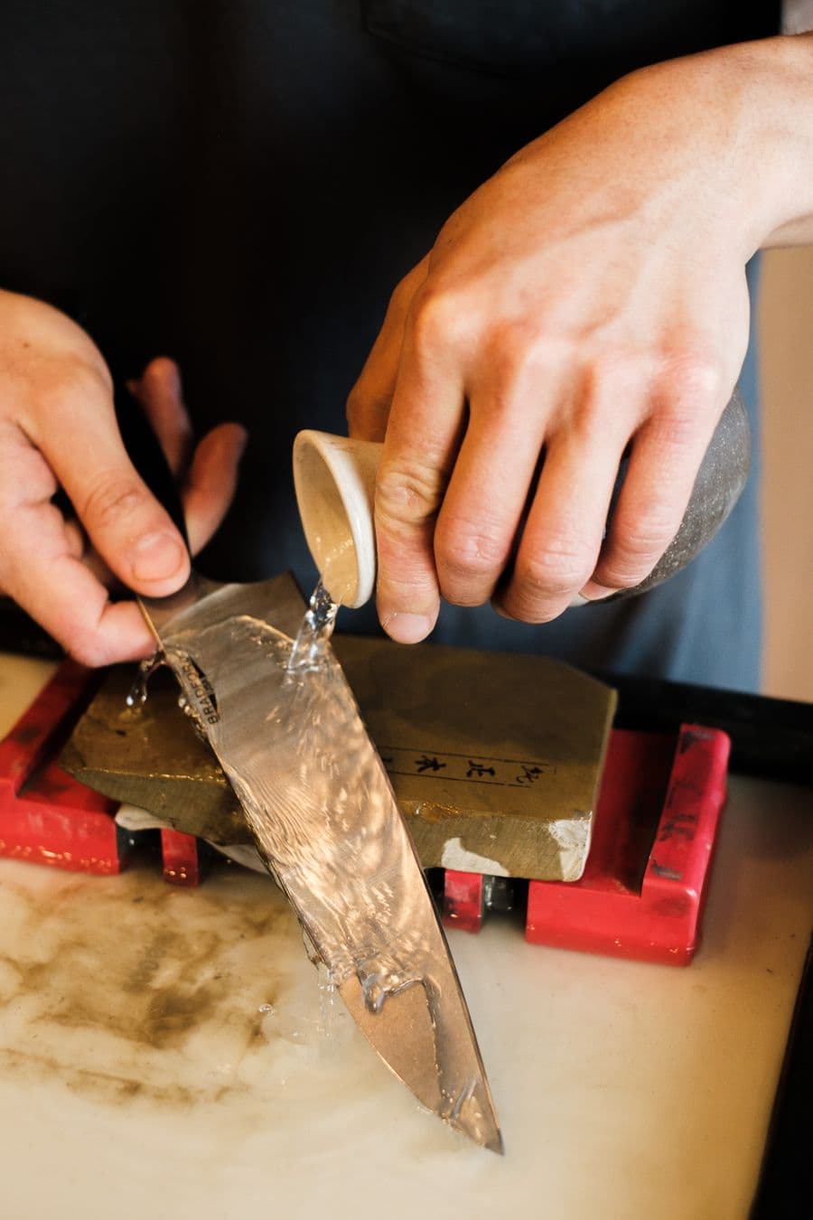 Hands sharpening a blade on a wet whetstone